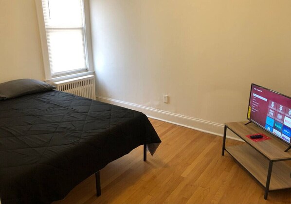 Ein Schlafzimmer mit einem Bett, einem Fernseher auf einem Schrank und einem Fenster mit Jalousien.