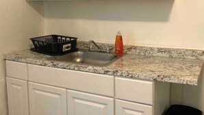 A kitchen with white cabinets, a granite countertop, a stainless steel sink, a black trash bin, and a dish soap bottle.