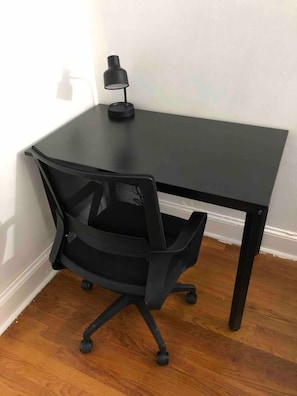 Mesa no canto com cadeira de escritório preta e abajur.