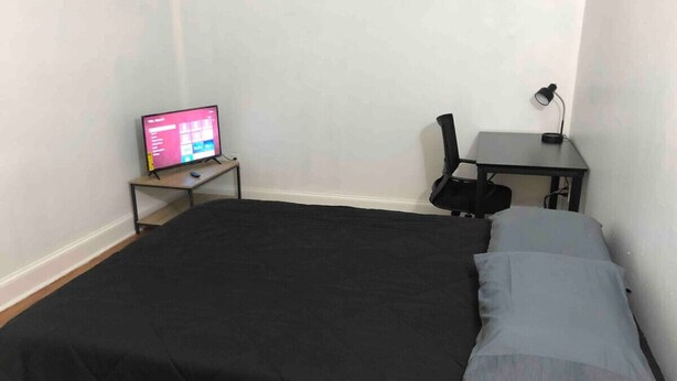 A room with a bed, a desk with a computer, and a lamp.