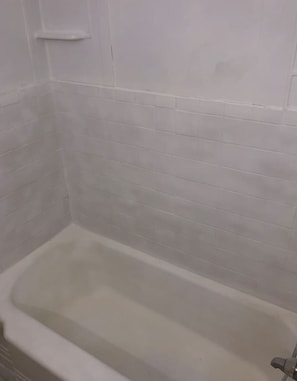 Uma banheira com parede revestida de azulejos brancos.