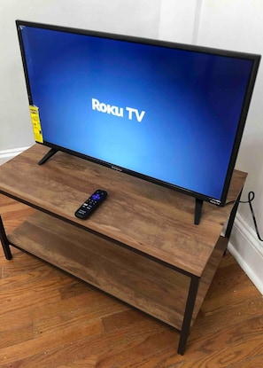 A flat-screen TV on a wooden stand with a remote control beside it.