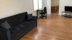 A living room with a dark-colored sofa, a wooden dining table with chairs, and a TV on a stand.