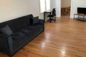 Ein Wohnzimmer mit einer dunkelgrauen Couch, einem Holzesstisch mit Stühlen und einem Fernseher auf einem Lowboard.
