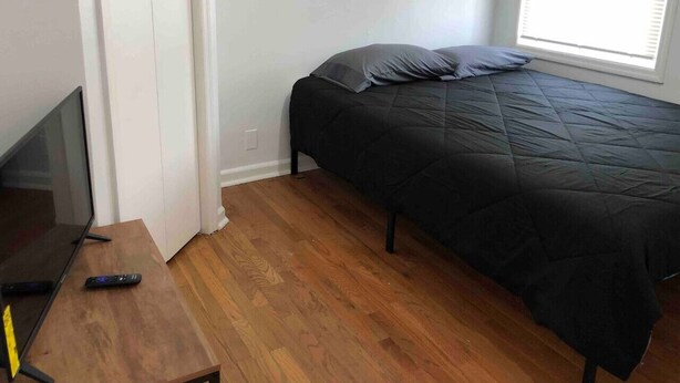 A bedroom with a bed, a TV, and a wooden floor.