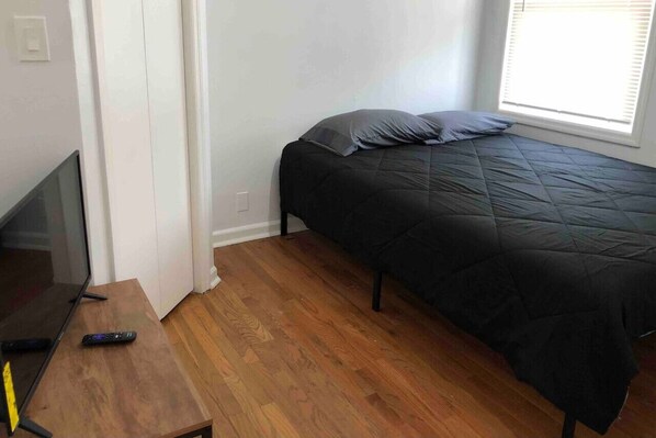 A bedroom with a bed, a TV, and a wooden floor.