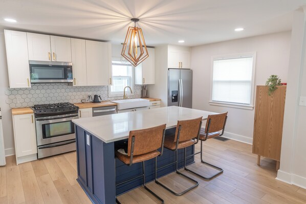 A modern kitchen with white cabinets, a central island with bar stools, a stainless steel refrigerator, and a hexagonal backsplash.