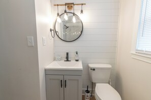 A bathroom with a round mirror, white sink, and toilet.