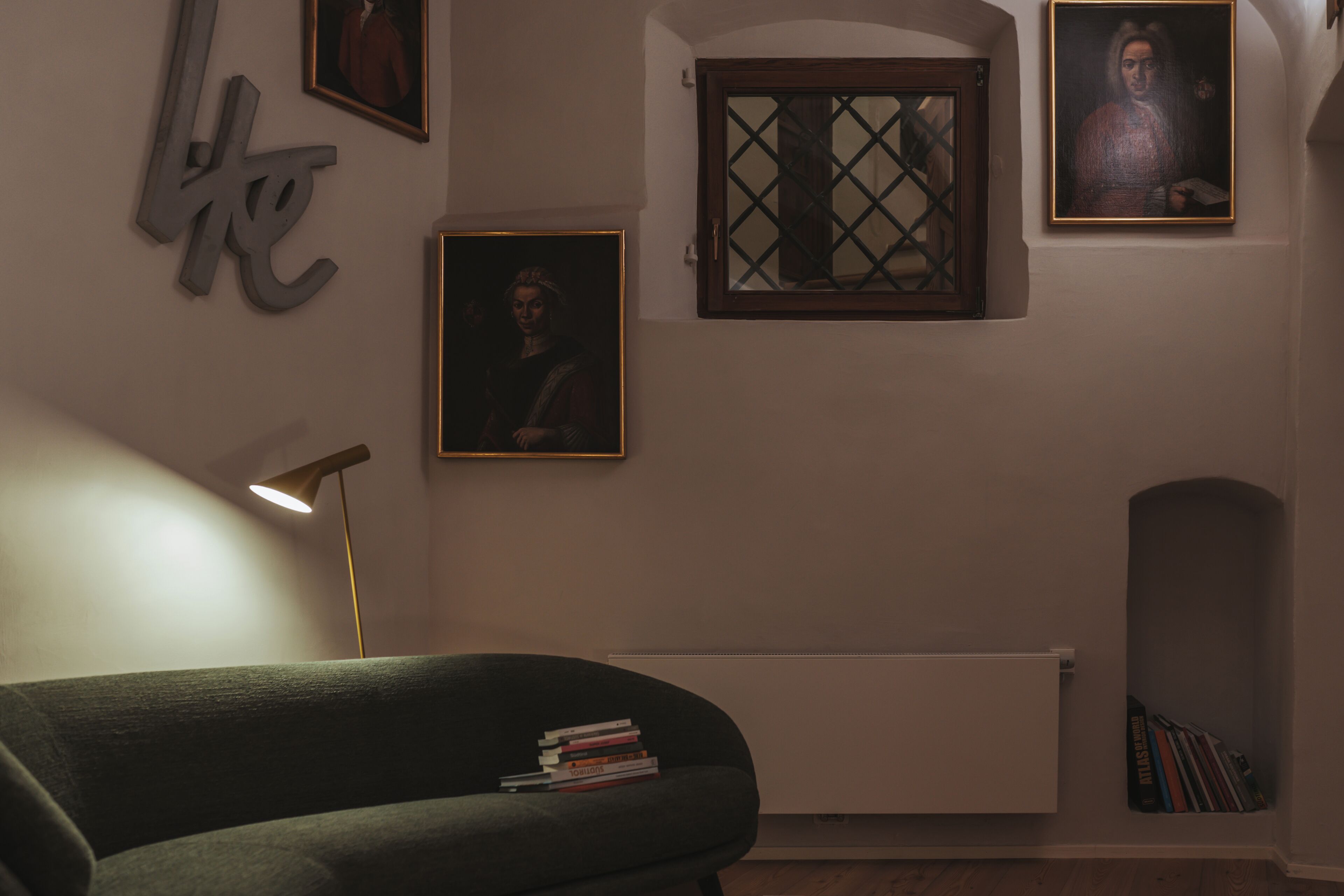 Ein Zimmer mit einem grünen Sofa, einem Heizkörper und gerahmten Bildern an der Wand.