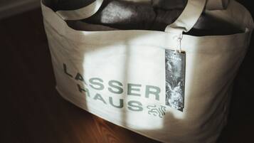 Una borsa porta tutto in tela beige con la scritta "LASSER HAUS", posata su un pavimento di legno.