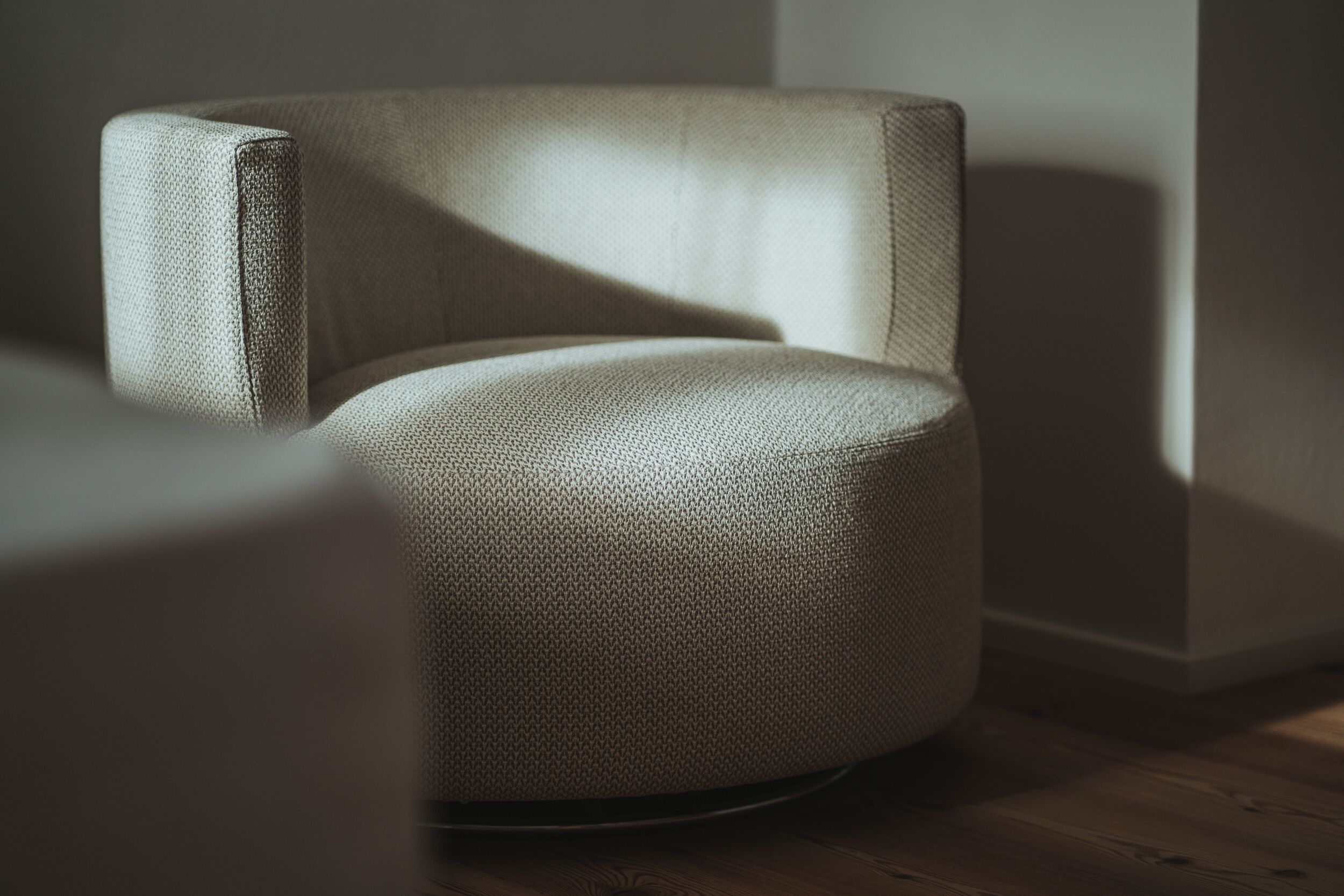 A modern, textured armchair in a minimalist room with a wooden floor and plain walls.