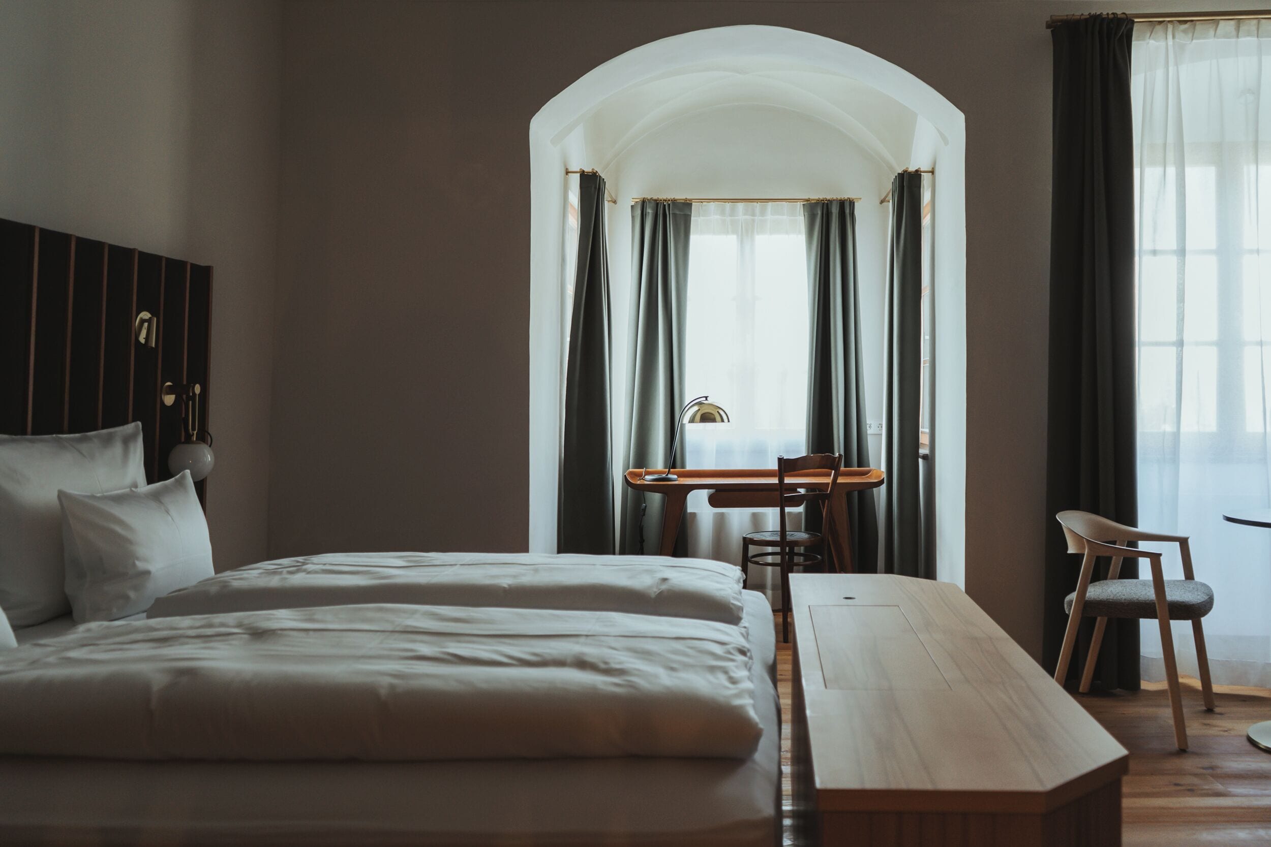 Une chambre d’hôtel avec un grand lit, un bureau et une chaise. Il y a une fenêtre avec des rideaux et une vue sur l’extérieur.