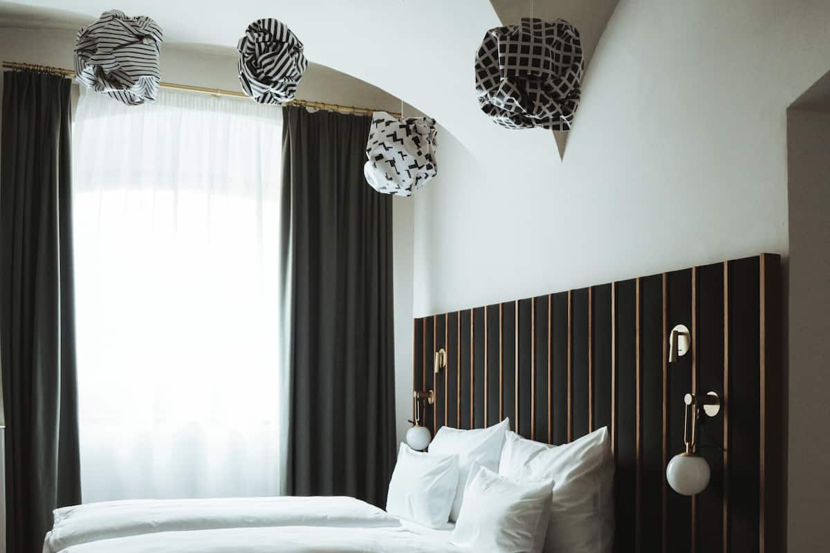 Ein Hotelzimmer mit Bett, Vorhängen, einem Kopfteil mit vertikalen Linien und hängenden Pendelleuchten.