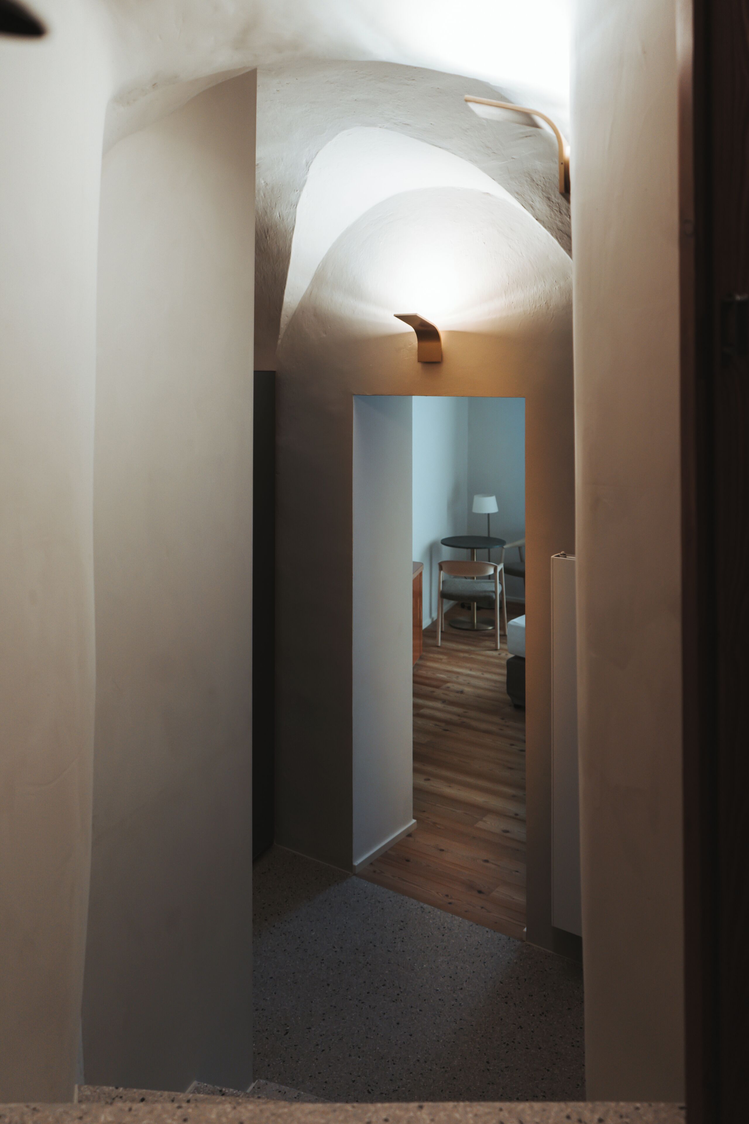 Un couloir étroit avec un plancher en bois, une chaise et une table sur laquelle se trouve une lampe.