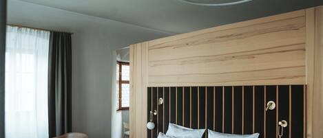 Una habitación de hotel moderna con un cabecero de madera, una cama con sábanas blancas, una silla y una ventana con cortinas.