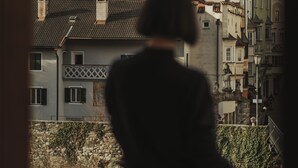 Una persona parada en un balcón con vistas a un pueblo con edificios históricos y dos torres destacadas.