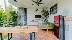 Una habitación con ventilador de techo, televisión, cama, una mesa con comida y un refrigerador.