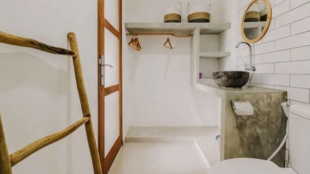 Un baño con una escalera de madera, un lavabo blanco con un recipiente, un espejo y repisas con artículos de tocador.