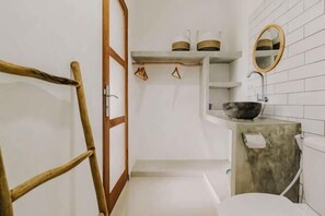 Un baño con una escalera de madera, un lavabo blanco con un recipiente, un espejo y repisas con artículos de tocador.