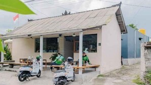 Un pequeño edificio con techo de láminas metálicas, un porche cubierto y dos scooters estacionados al frente.
