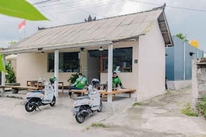 Pieni rakennus, jossa on aaltopeltikatto, katettu kuisti ja sen edessä parkkeerattuina kaksi skootteria.