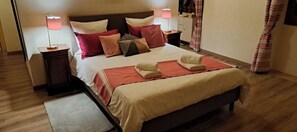 Un lit bien fait, recouvert d’une couvre-lit rouge et beige, avec deux lampes de chevet et un plancher en bois.