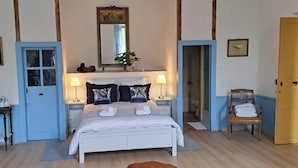 Un dormitorio con cama, mesitas de noche, una silla, una puerta y un espejo.