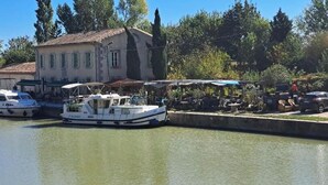 Un canal con barcos amarrados, un edificio de techo con tejas y árboles al fondo.