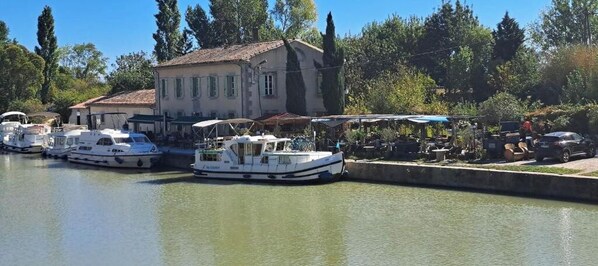 Un canal où sont amarrés des bateaux, un bâtiment avec un toit en tuiles et des arbres en arrière-plan.