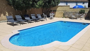 Una piscina rectangular con un borde de baldosas, rodeada de sillas de descanso y una mesa.