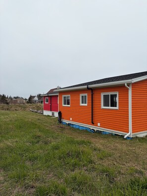 A row of two single-story buildings with a flat roof, white trim, and a grassy field in the foreground.