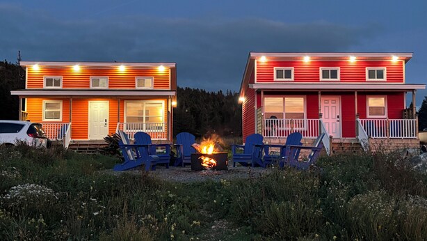Zwei Hütten mit jeweils einer Veranda, einer Feuerstelle und blauen Adirondack-Stühlen.