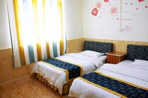 A hotel room with two beds, wooden flooring, and a window with curtains.