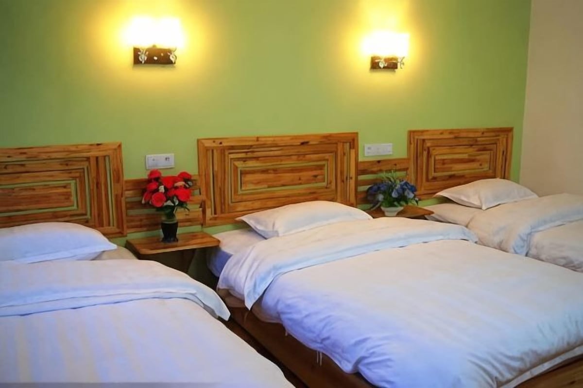 A hotel room with two beds, wooden headboards, bedside tables with lamps, and wall-mounted light fixtures.
