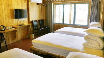 A room with two beds, a desk with a chair, a television, and a window with curtains.