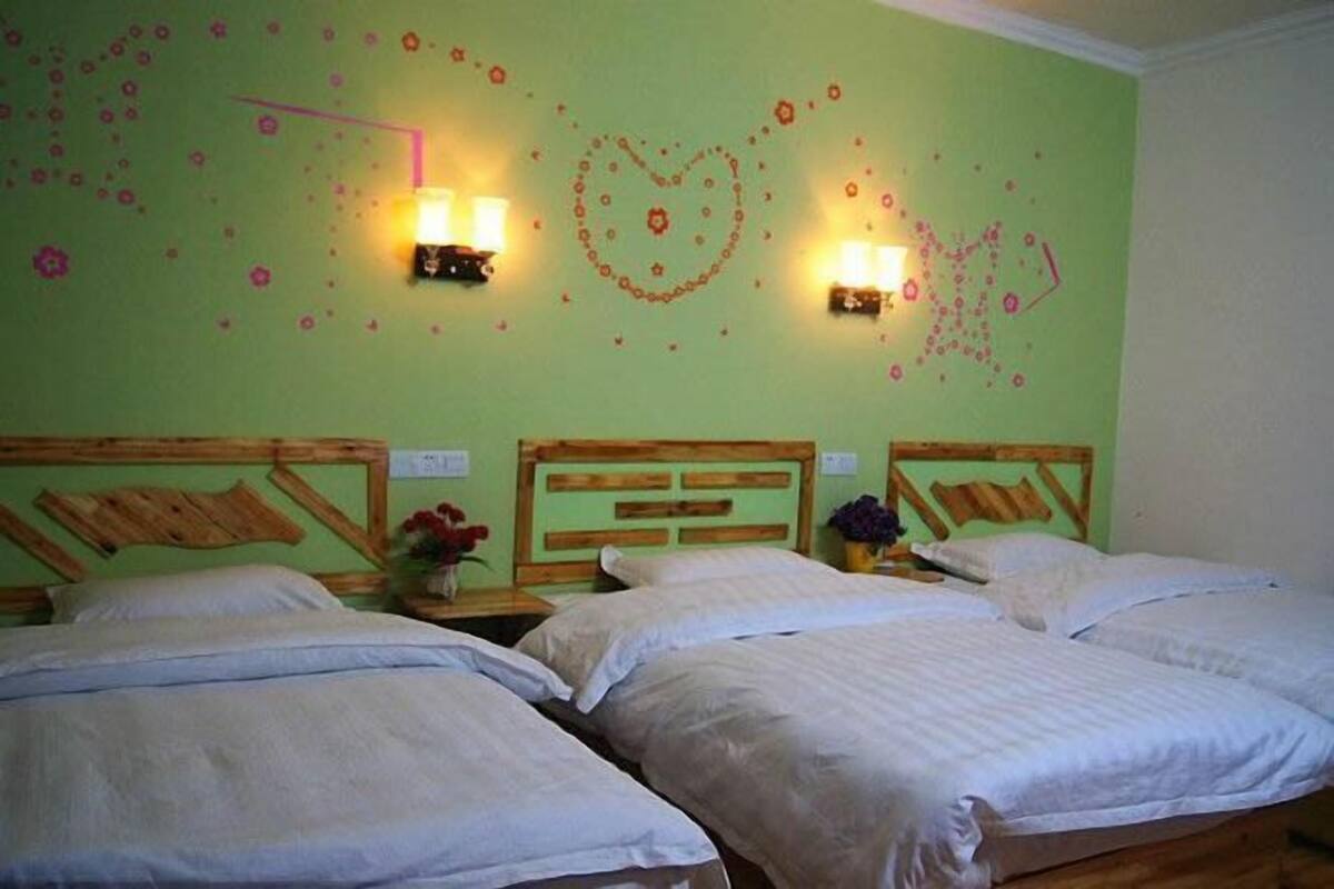Une chambre avec trois lits, chacun doté de draps blancs, d’une tête de lit en bois et de deux lampes fixées au mur.