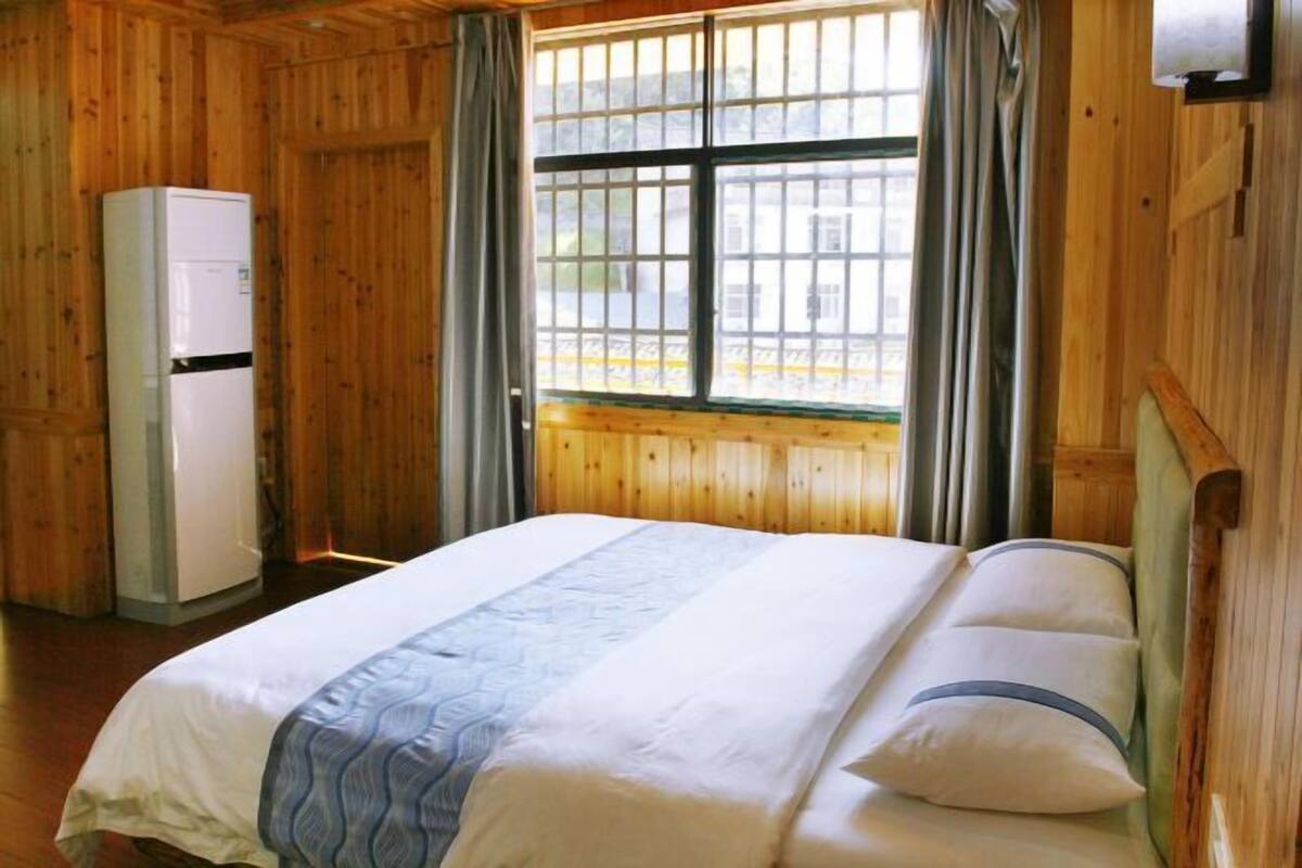Une pièce de cabane en bois comprenant un lit, une fenêtre avec des rideaux et un réfrigérateur.