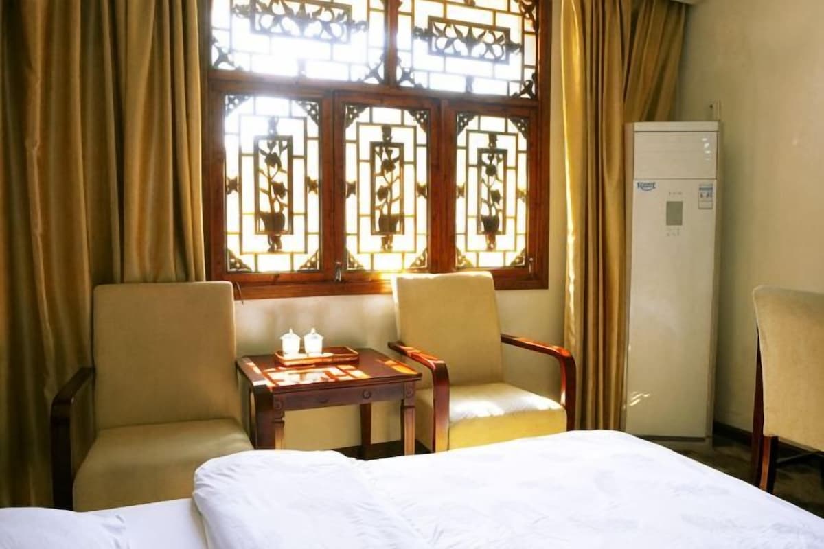 A hotel room with a bed, two chairs, a small table with a teapot, and a refrigerator.