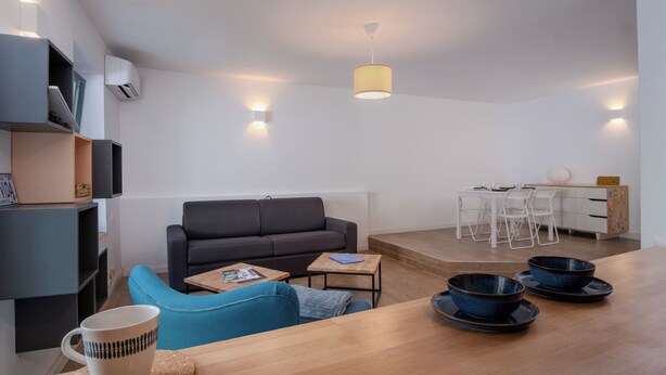 A modern living room with a sofa, coffee table, and dining area with a table and chairs.