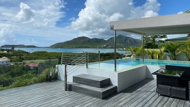 A modern outdoor pool area with a view of the sea and mountains.