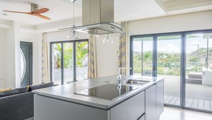 A modern kitchen with a central island, large windows, and a view of greenery.