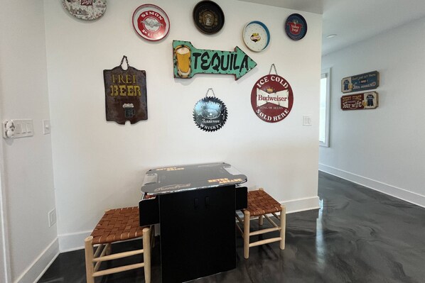 Une pièce avec une table noire et deux chaises, un mur décoré de divers objets sur le thème de la bière, et un plancher en bois foncé.
