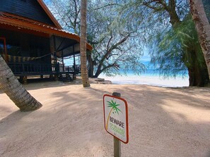 A beachside area with a warning sign about falling coconuts, a wooden structure, and a view of the ocean. - Sairee Cottage Resort (Koh Tao)