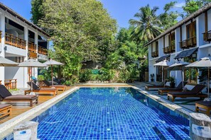 A pool area with lounge chairs and umbrellas, surrounded by lush greenery and a building with multiple balconies. - Sairee Cottage Resort (Koh Tao)