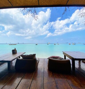 A wooden deck with two tables and two cushioned seating areas overlooking a calm sea with boats. - Sairee Cottage Resort (Koh Tao)