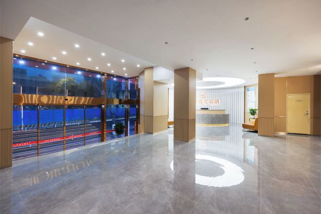A modern hotel lobby with a reception desk, a large window with a view of the street, and a clean, polished floor.