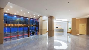 A spacious lobby with a reflective floor, a reception desk, and a large glass wall with a view of the outside.