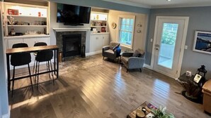A spacious living room with a fireplace, a dining area with a table and chairs, and a kitchen area with a TV. - Melancy waterfront cottage in Sainte-Agathe Nord (Ivry-sur-le-Lac).  (Sainte-Agathe Nord)