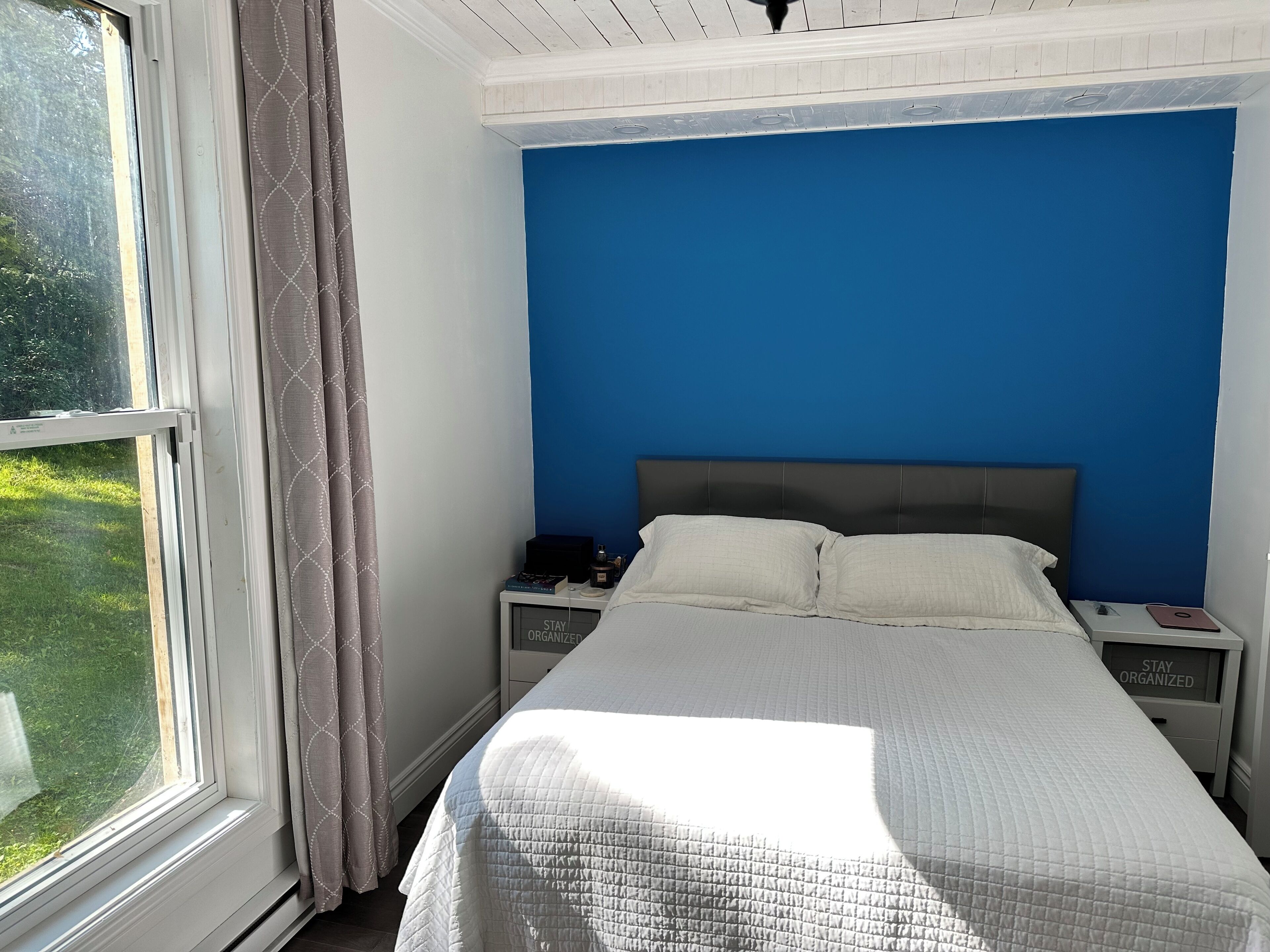 A bedroom with a bed, a nightstand, a window, and a view of greenery outside.