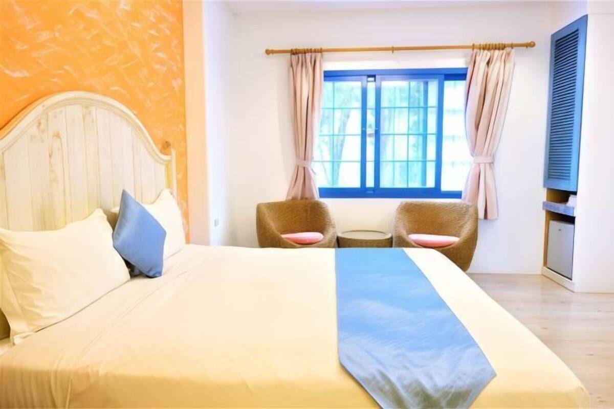 A bed with pillows, a bedside table, a window with curtains, and a chair.